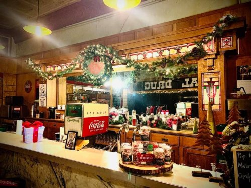 A vintage drugstore counter decorated for the holidays, featuring garlands, Coca-Cola signage, and festive gifts.