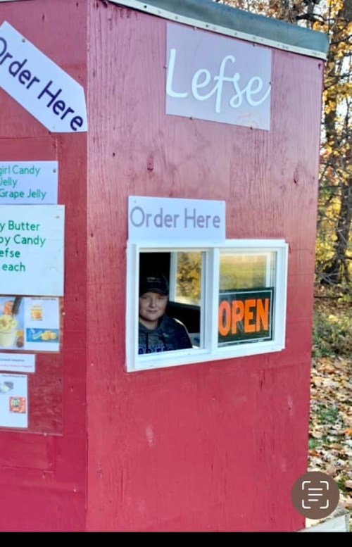 A small red stand with a window, featuring a sign that says "Order Here" and a person inside, with an "OPEN" sign visible.
