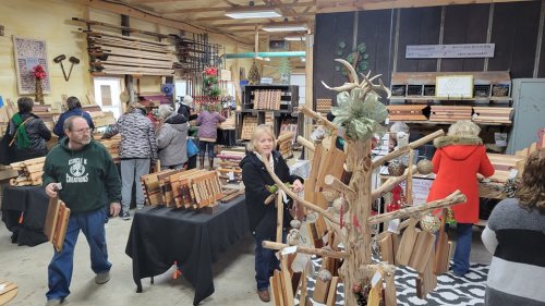 A busy woodworking shop with people browsing wooden items and a decorative tree made of cutting boards.