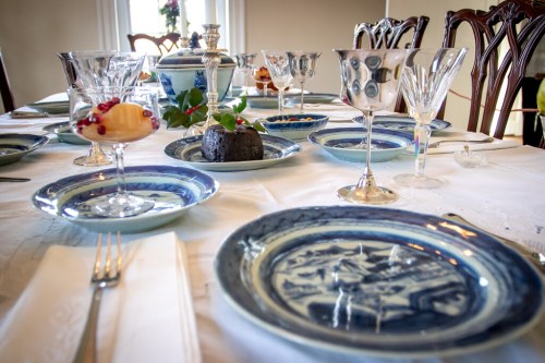 A beautifully set dining table with elegant glassware, decorative plates, and a centerpiece of fruit and dessert.