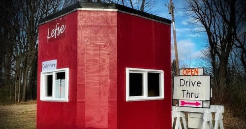A small red drive-thru booth with "Lefse" sign, open for orders, surrounded by trees.