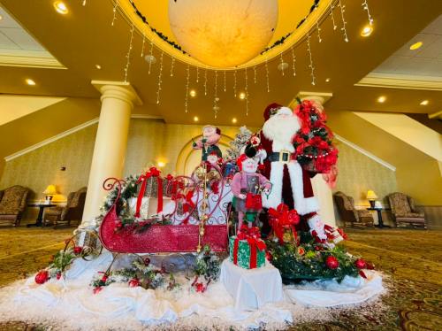 A festive holiday display featuring Santa, elves, a decorated sleigh, and Christmas decorations in a cozy lobby.
