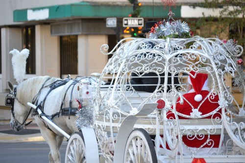 A decorated white horse-drawn carriage with a Santa figure inside, surrounded by festive ornaments.