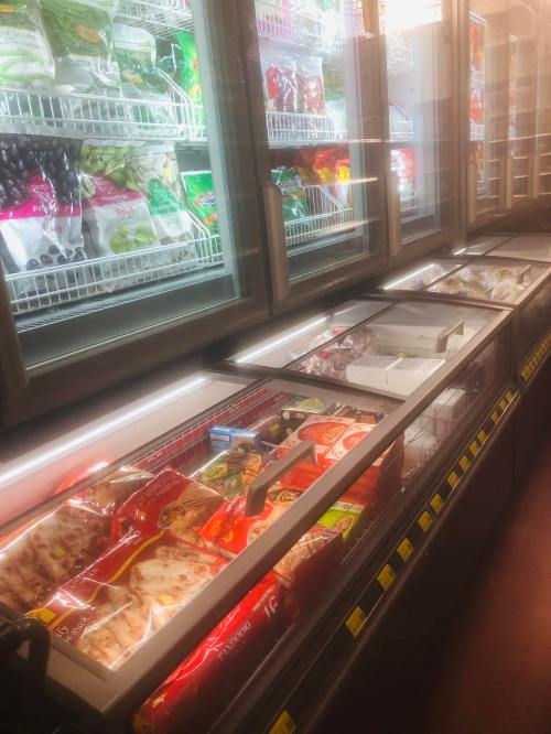 A grocery store freezer section filled with various frozen food items, including pizzas and vegetables.