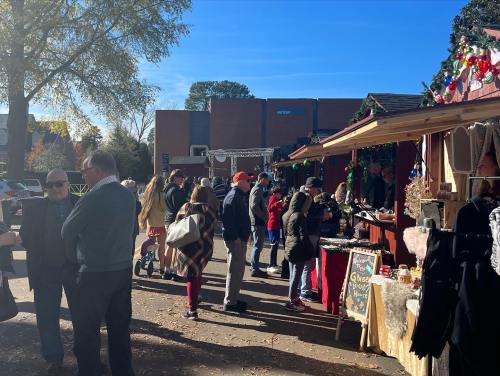 A bustling outdoor market scene with people browsing stalls under a clear blue sky, decorated for the season.