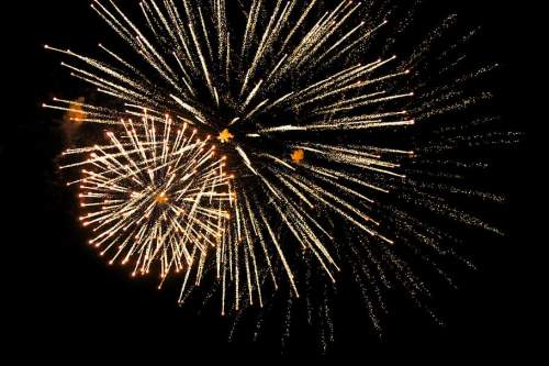 Colorful fireworks explode in the night sky, creating vibrant bursts and trails of light against a dark background.