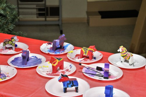 Colorful painted figurines on paper plates, with paintbrushes, on a red tablecloth in a creative setting.
