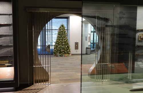 A festive Christmas tree is visible through a large, decorative archway in a modern museum space.