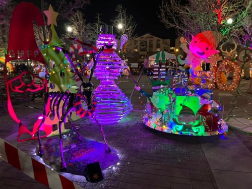 Colorful holiday decorations featuring a snowman, reindeer, and whimsical characters, illuminated at night.