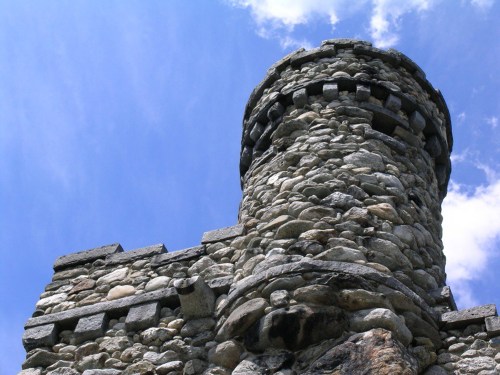 A stone castle tower against a blue sky with scattered clouds.