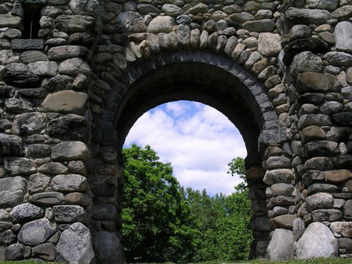 Stone archway with a view of green trees and a blue sky in the background.