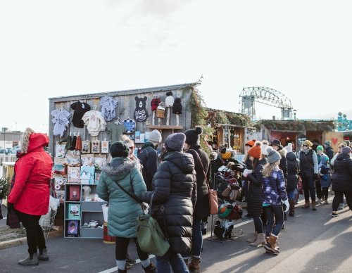 A bustling outdoor market with people browsing handmade goods and festive decorations on a chilly day.