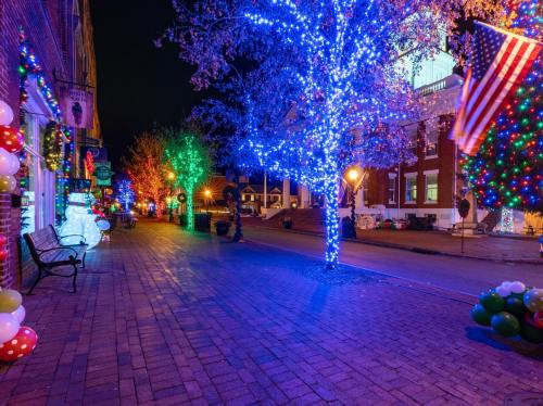 A festive street scene at night, adorned with colorful holiday lights and decorations, including an American flag.
