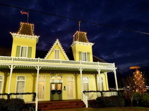 A yellow house with festive lights and decorations, set against a dark, cloudy evening sky.