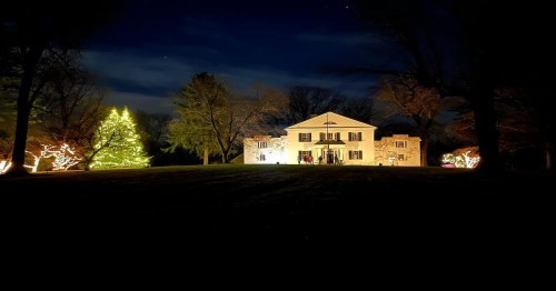 A beautifully lit house at night, surrounded by trees and a large decorated Christmas tree.