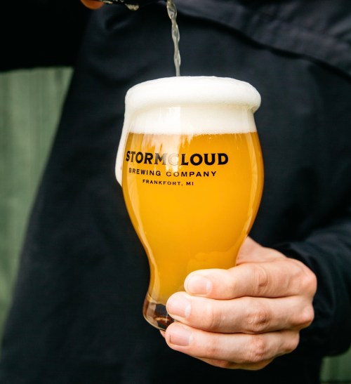A person pours beer into a glass with the logo of Stormcloud Brewing Company, showcasing a frothy, golden beverage.