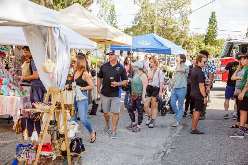 A bustling outdoor market scene with people browsing stalls and tents filled with various goods and crafts.
