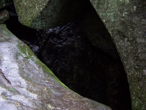 A dark crevice between large, moss-covered rocks, with wet surfaces reflecting light.