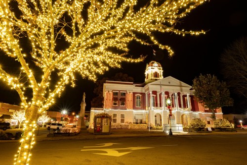 A beautifully lit historic building at night, adorned with festive lights, surrounded by a glowing tree.