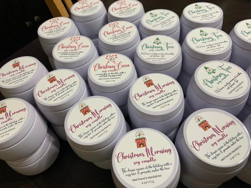 A collection of scented candle jars with festive labels, including "Christmas Wornings," "Christmas Tree," and "Christmas Cocoa."