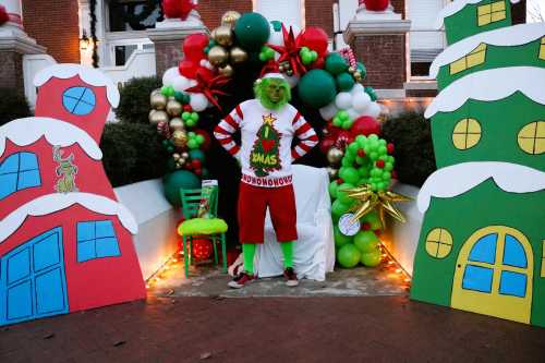 A festive scene featuring a person dressed as the Grinch, surrounded by colorful holiday decorations and oversized gift boxes.