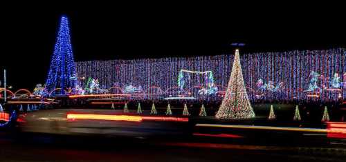 Colorful holiday lights illuminate a dark scene, featuring trees, decorations, and festive displays along a road.