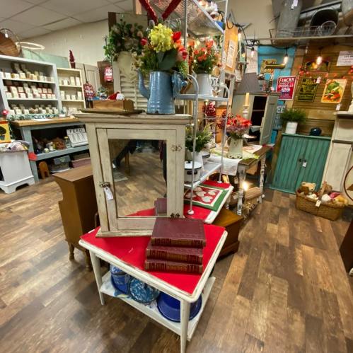 A vintage-style display featuring a small mirror cabinet, books, and decorative items in a cozy shop setting.