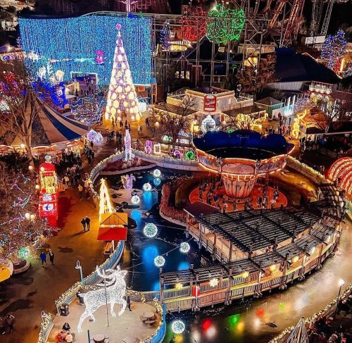 Aerial view of a festive amusement park decorated with colorful lights, a Christmas tree, and a carousel.