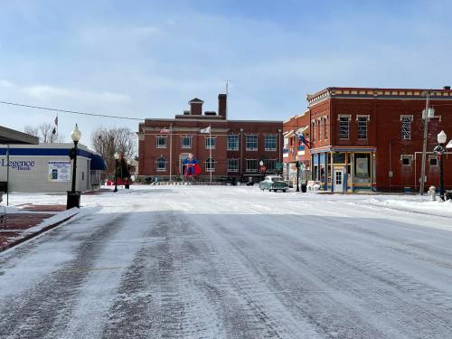 Snow-covered street scene with historic buildings and a bank, under a clear blue sky.
