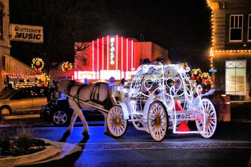 A lit-up horse-drawn carriage moves through a festive street at night, with colorful lights and decorations in the background.