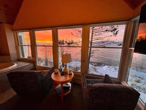 Cozy seating area with two chairs and a table, overlooking a vibrant sunset over the water through large windows.