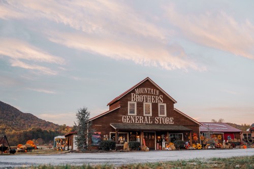 A rustic general store with "Mountain Brothers" sign, surrounded by mountains and a colorful autumn landscape.