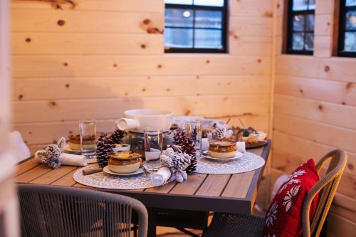 A cozy dining table set with dishes, glasses, and pinecone decorations in a warmly lit wooden room.