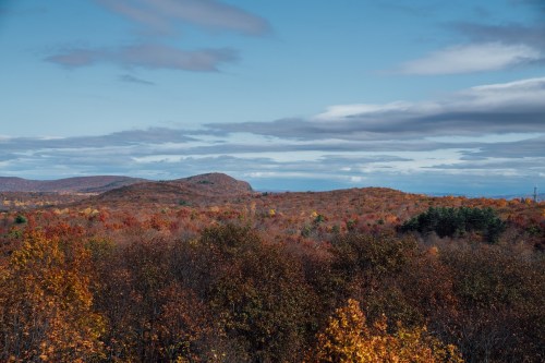 A scenic view of rolling hills covered in vibrant autumn foliage under a blue sky with scattered clouds.