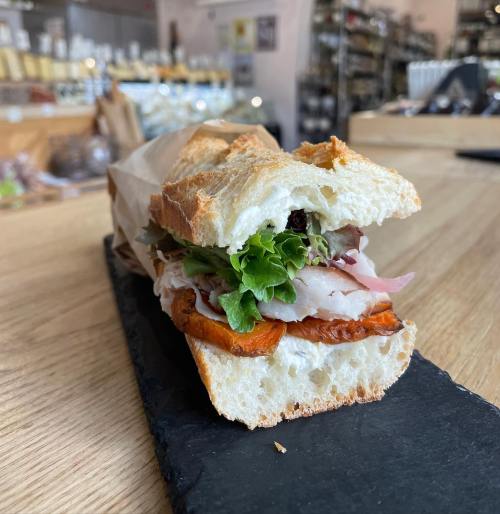 A fresh sandwich with turkey, lettuce, and roasted peppers, served on a rustic wooden table.