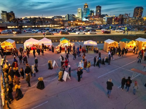 A bustling outdoor market at dusk, with festive tents, lights, and crowds enjoying the atmosphere in a city setting.