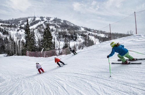 A group of children skiing down a snowy slope with trees and a mountain in the background.