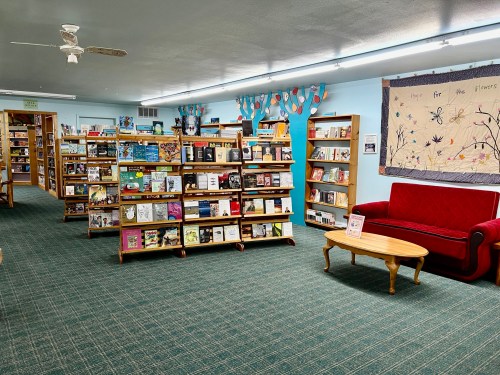 A cozy library interior with bookshelves, a red couch, and a quilted wall hanging.