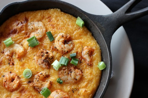 A cast iron skillet filled with cheesy shrimp and grits, topped with green onions.