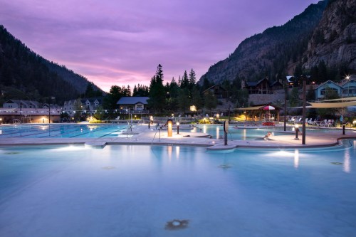A serene outdoor pool surrounded by mountains at sunset, with soft lighting and a tranquil atmosphere.