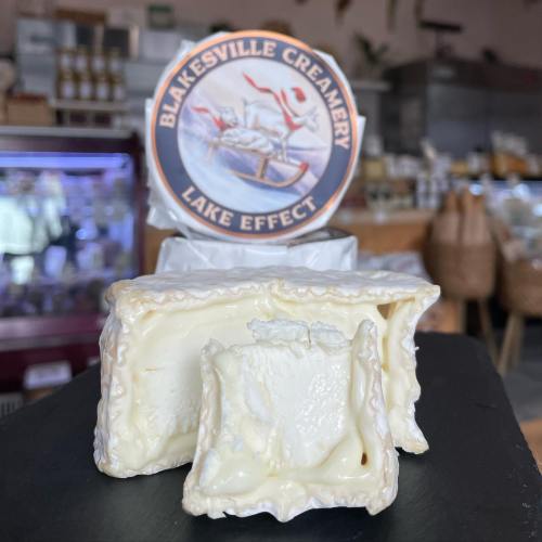 A round cheese wheel with a creamy texture, labeled "Blakesville Creamery Lake Effect," displayed on a black surface.
