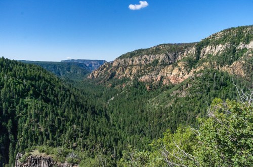 A panoramic view of lush green mountains and cliffs under a clear blue sky, showcasing a vibrant natural landscape.