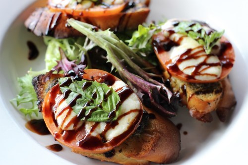 Bruschetta topped with tomato, mozzarella, and basil drizzled with balsamic glaze, served on a bed of greens.