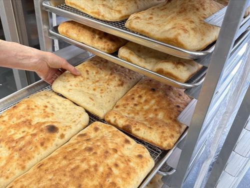 A hand reaches for a freshly baked loaf of bread on a rack filled with golden-brown, crusty flatbreads.