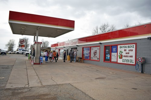 A convenience store with a gas station, featuring a group of people outside and signage for food options.