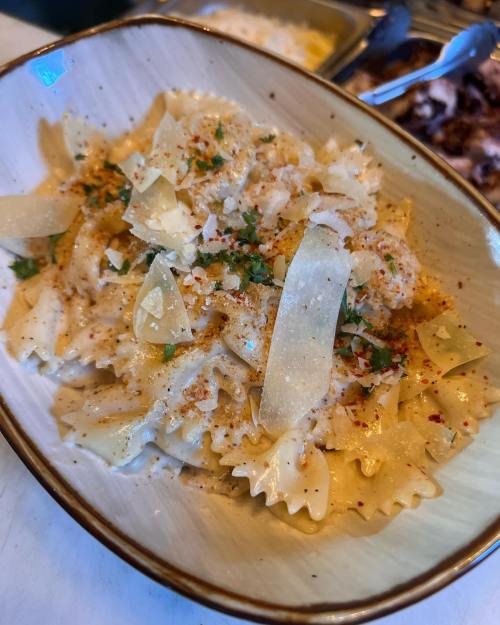 A bowl of farfalle pasta topped with cheese, herbs, and spices, served in a light-colored dish.