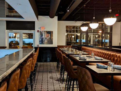 Modern restaurant interior with leather seating, elegant tables, and large windows, featuring a stylish bar area.