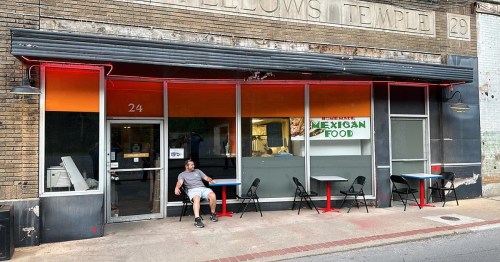 A man sits outside a Mexican restaurant with red and blue tables, featuring a sign that reads "Authentic Mexican Food."