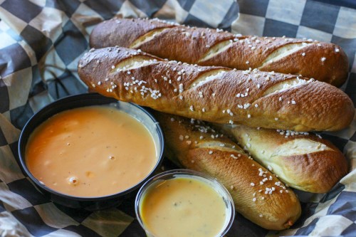 A basket of soft pretzels with coarse salt, accompanied by two bowls of cheese dip.
