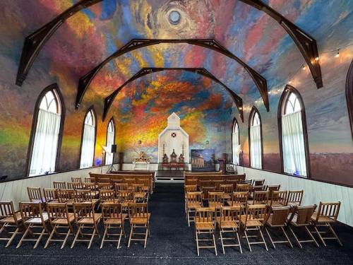 A colorful, mural-adorned chapel interior with wooden chairs arranged for a gathering.